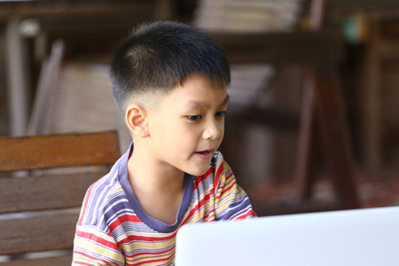 A young boy is engaged in learning on a laptop, showcasing curiosity and focus in a casual home environment. His colorful striped shirt adds vibrancy to the scene.の写真素材