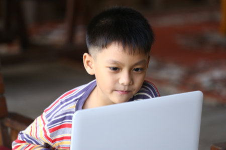 A young boy is intently focused on a laptop, engaging in learning or entertainment. This scene captures the essence of childhood curiosity and modern technology.の写真素材
