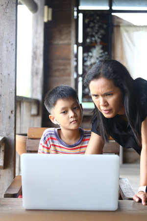 A mother and her child engage with a laptop, immersed in learning at home. The scene captures the...