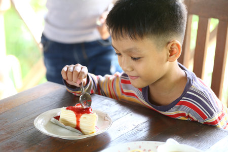 A young boy relishes a slice of cake topped with strawberry sauce, capturing the joy of dessert. Perfect for celebrating sweet moments with family.の写真素材