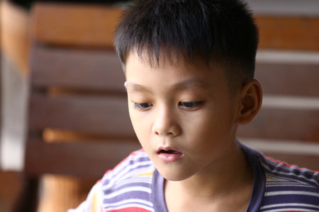 A thoughtful young boy with a focused expression gazes into the distance, showcasing innocence and curiosity in a casual striped shirt, captured in natural light.の写真素材