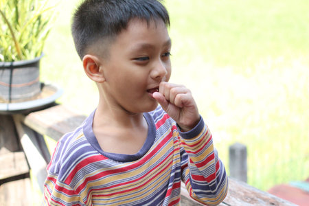 A young boy is seen sucking his thumb in a bright outdoor setting, embodying a sense of innocence...