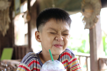 A joyful child with a playful expression enjoys a colorful drink in a cozy indoor setting. This charming portrait captures the essence of childhood happiness.の写真素材