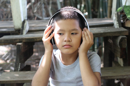 A young boy wearing headphones enjoys music in a serene outdoor setting. He expresses focus and joy...