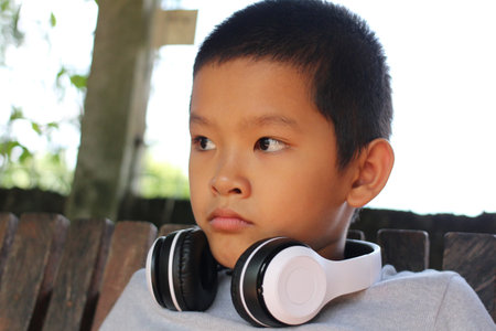 A thoughtful boy wearing headphones sits in an outdoor setting, lost in his music. The image...