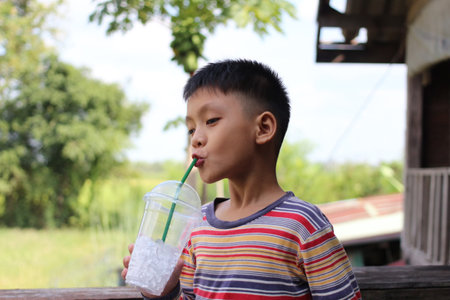 A cheerful young boy enjoys a refreshing drink with ice while surrounded by nature, capturing a moment of joy and childhood innocence on a warm day.の写真素材