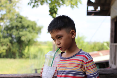 A young boy enjoys a refreshing drink while sitting outdoors. The vibrant environment captures a joyful moment filled with sunshine and natural beauty.の写真素材