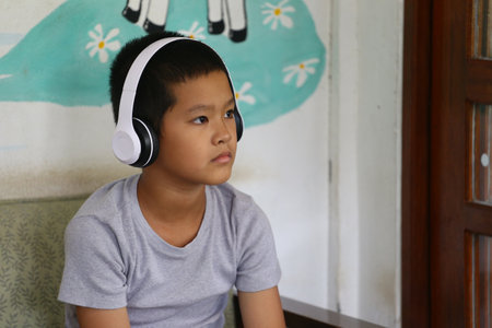 A serene boy sits indoors, immersed in his music while wearing headphones. His focused expression captures a moment of relaxation and creativity.の写真素材