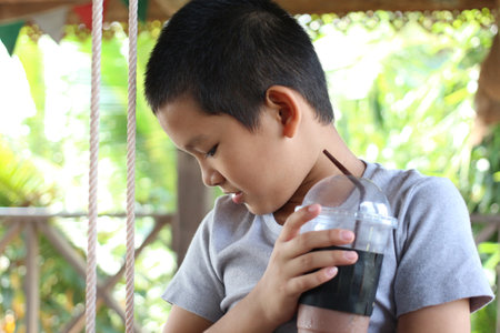 A young boy enjoys a refreshing drink while sitting on a swing in a vibrant outdoor setting, embodying the joys of childhood and nature.の写真素材