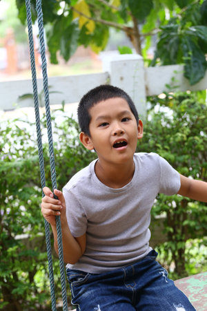 A young boy on a swing in a bright park, showcasing the joy of childhood. His expression captures...