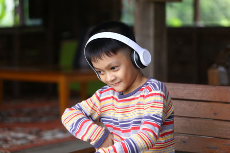 A young boy wearing headphones smiles while enjoying music in a cozy indoor setting, embodying joy and innocence. Perfect for lifestyle themes.の写真素材