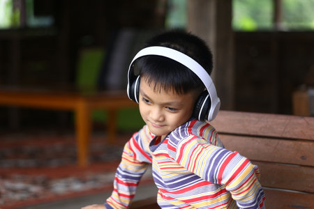 A joyful child enjoys music with headphones while sitting comfortably indoors. The playful expression and colorful striped shirt capture a moment of youthful happiness and relaxation.の写真素材