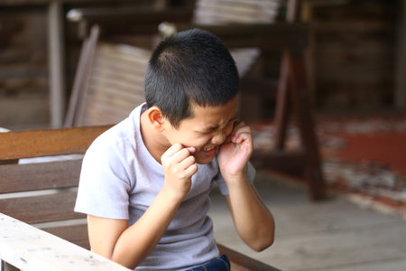 A young boy sits outdoors, making a funny face that captures pure joy and innocence. His playful expression brings a sense of happiness to the scene.の写真素材