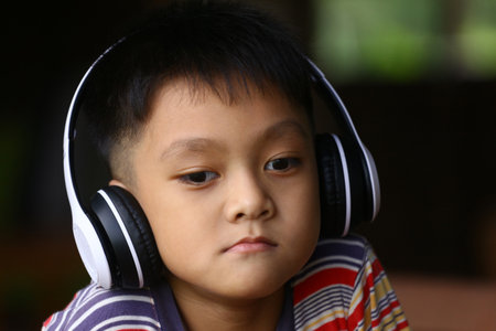 A young boy sits quietly with headphones on, deeply immersed in his music. His relaxed expression captures the joy of listening, showcasing childhood moments.の写真素材