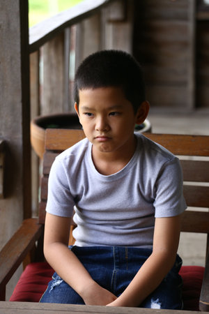 A young boy sits alone in a rustic indoor setting, displaying a thoughtful expression. The calm atmosphere emphasizes the emotion of solitude and reflection.の写真素材