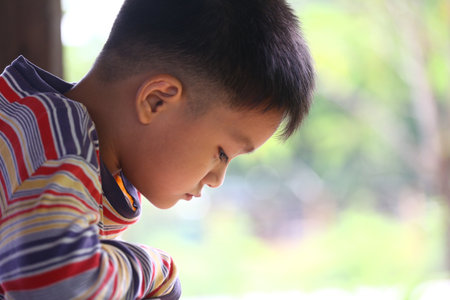 A young boy is captured in profile, deep in thought. The serene outdoor background adds to the peaceful atmosphere, showcasing the beauty of childhood reflection.の写真素材