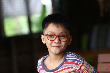 A cheerful young boy with glasses poses in a casual indoor setting, showcasing his playful spirit and joyful personality. Bright colors and warm light enhance the captivating atmosphere.の写真素材