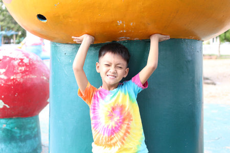 A joyful child enjoys a colorful playground, smiling while playfully holding onto a vibrant structure. Perfect for themes of childhood and outdoor fun.の写真素材