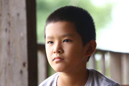 A close-up portrait of a thoughtful boy sitting in a serene environment. The natural light highlights his expression and features, evoking a sense of innocence and calm.の写真素材