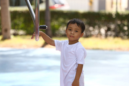 A young boy in a white shirt enjoys a playful moment outdoors at a park, surrounded by sunlight. His expression captures the essence of childhood joy and freedom in a natural environment.の写真素材