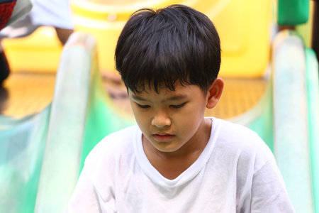A young boy absorbed in thought on a colorful playground slide, embodying childhood innocence. The...