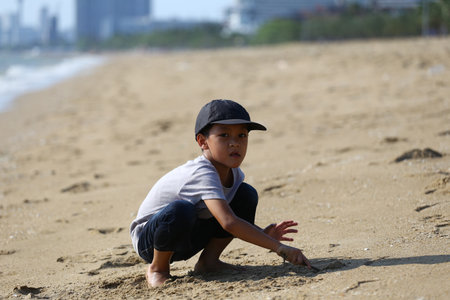 A young boy experiences the joy of playing in the sand on a sunny beach, exploring the textures of his surroundings while enjoying the beauty of nature.の写真素材