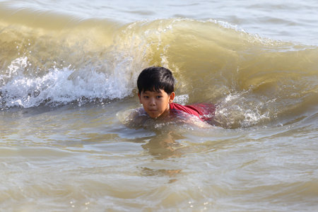 A young boy swims in ocean waves, capturing a joyful moment of playfulness and adventure during a sunny day at the beach. Perfect for summer-themed visuals.の写真素材