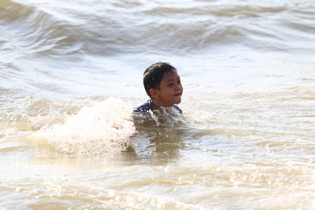 A young boy splashes joyfully in the shallow waters of a beach, embodying the carefree spirit of childhood and the warmth of a sunny summer day by the ocean.の写真素材