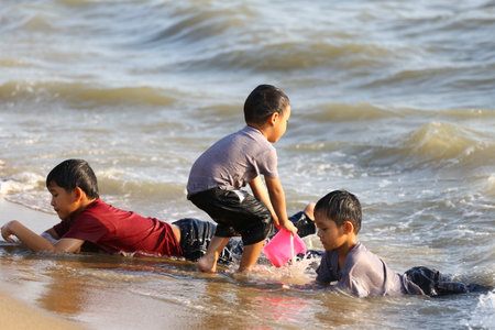 Three children engage in joyful play on a sunlit beach, splashing water and creating cherished memories. Their laughter reflects the carefree spirit of summer days by the ocean.の写真素材