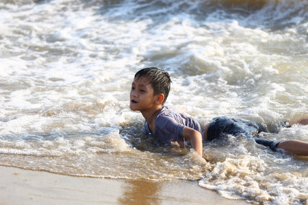 A young boy experiences the fun of playing in the ocean waves on a sunny day, embodying the carefree spirit of childhood during a memorable beach outing.の写真素材