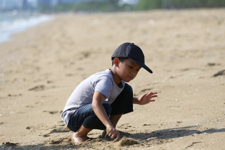 A young boy interacts with soft sand on a beautiful beach, capturing the essence of childhood joy, curiosity, and the wonder of outdoor exploration beneath the sun.の写真素材