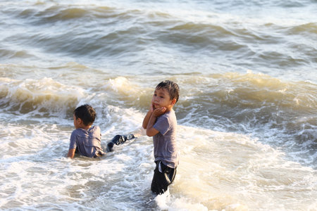 Two young boys play joyfully in the shallow ocean waters, surrounded by gentle waves and sunlight, capturing the essence of childhood happiness and adventure.の写真素材