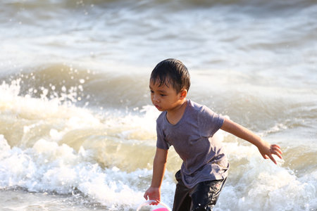 A young boy is playing at the beach, splashing in the waves with joy and curiosity. This image captures the essence of childhood fun and the beauty of a day by the shore.の写真素材