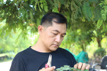 A focused man uses pruning shears to care for plants in a lush green environment, showcasing dedication to gardening and nurturing nature's beauty.の写真素材