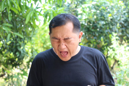A man expressing a strong emotion outdoors surrounded by lush greenery. His candid reaction captures...