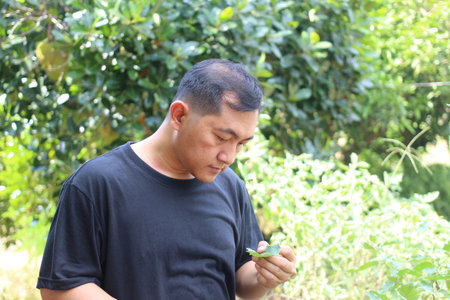 A man is closely examining a green leaf in a vibrant garden. The scene reflects a connection with...