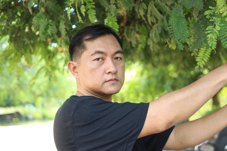 A man stands amidst lush greenery, interacting with nature in a serene outdoor setting. His calm...