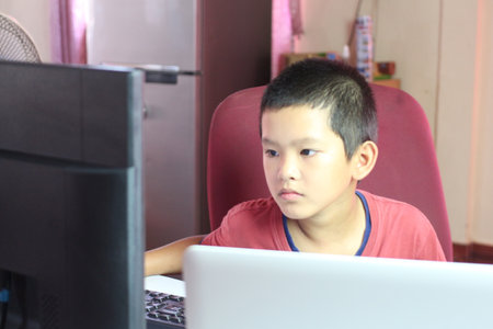 A young boy sits attentively at a desk, engaged with a computer screen. Capturing a moment of...