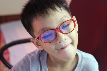 A young boy wearing red glasses is captured in a moment of thoughtfulness, reflecting innocence and...