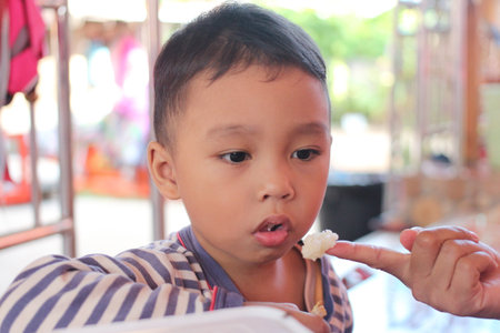 A young child shows curiosity while tasting food. Capturing a moment of innocence and joy, this image illustrates a delightful dining experience.の写真素材