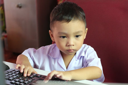 A young boy engaged in using a computer, showcasing focus and concentration. This image captures the essence of learning and technology in a modern environment.の写真素材
