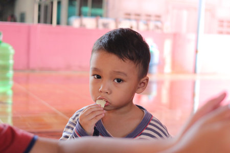 A young boy enjoys a snack in a well-lit indoor environment. His curious expression captures a moment of childhood joy and innocence.の写真素材