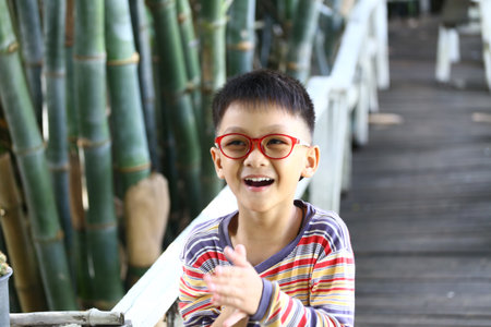 A smiling child with glasses enjoys the outdoors surrounded by bamboo. His joyful expression captures the essence of childhood and carefree moments.の写真素材