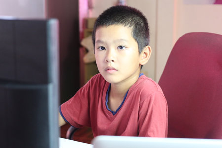 A young boy sits at a desk, intently focused on the computer screen, showcasing concentration in a modern home workspace environment.の写真素材