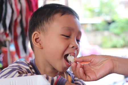 A joyful child savoring a snack outdoors, showcasing innocent delight in sharing food. This image captures the essence of childhood happiness and cultural moments.の写真素材