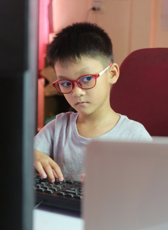 A young child wearing glasses concentrates on a computer screen in a home office setting. This image captures the essence of learning and technology.の写真素材