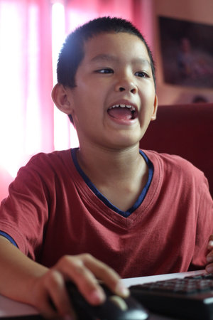 A joyful boy engaged in computer activities, showcasing his enthusiasm. The image captures a moment of innocence and curiosity in a home setting.の写真素材