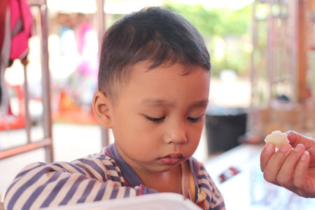 A thoughtful young boy in striped pajamas focuses on a snack, showcasing a moment of innocence and joy in a casual outdoor setting.の写真素材