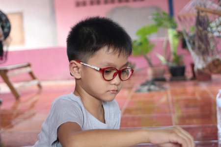 A young boy with glasses sits quietly indoors, focused on his play. The colorful setting and relaxed atmosphere highlight his curious personality and innocence.の写真素材