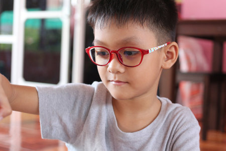 A young child wearing vibrant glasses engages in a fun indoor activity. His focused expression showcases curiosity and joy, reflecting childhood innocence.の写真素材